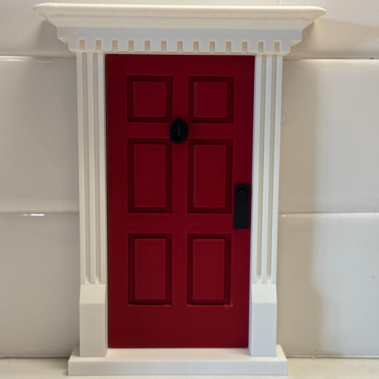 Miniature red door with white trim displayed on counter – perfect for holiday elf scenes or kids’ play areas