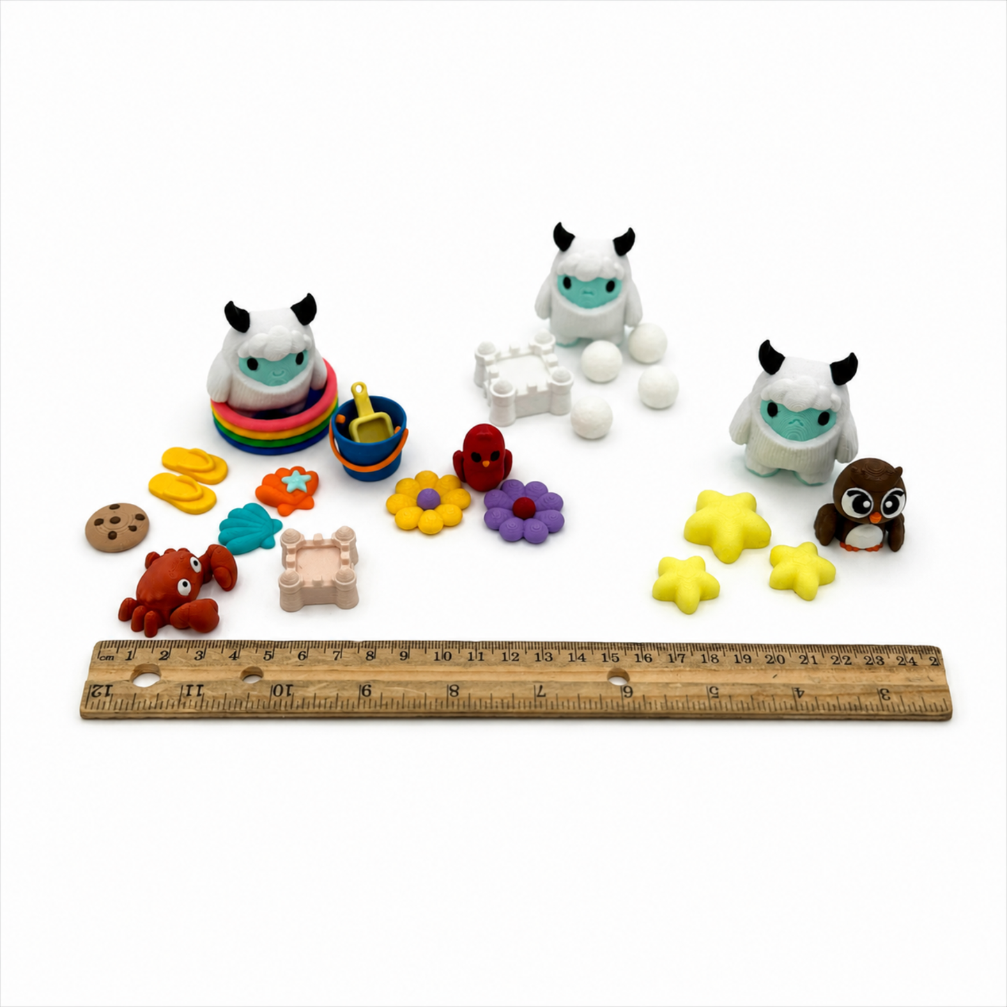 Yeti & Friends sensory play set shown beside a ruler for size reference, including miniature yetis, beach accessories, flowers, stars, owl, and crab for storybook extension activities.