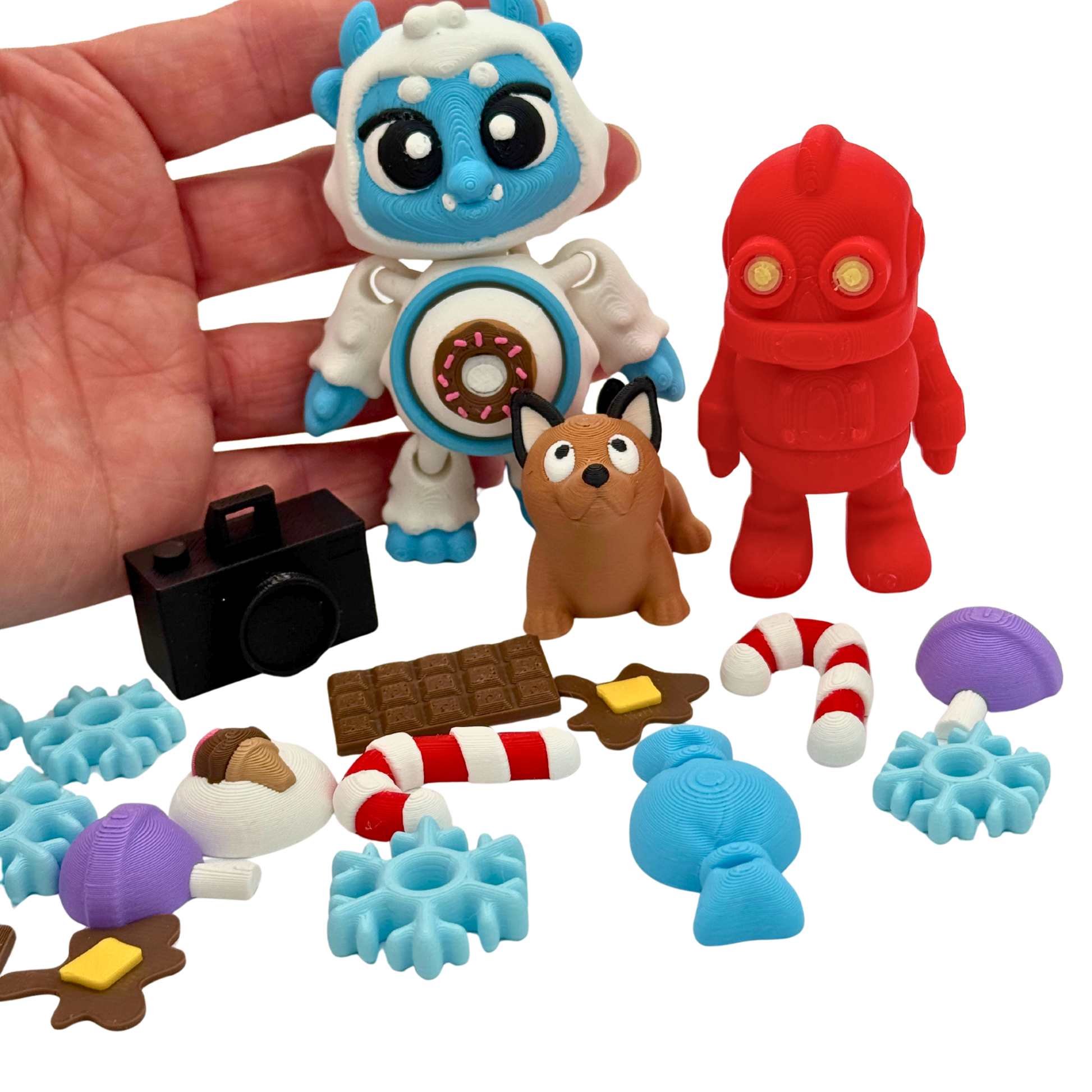 Hand holding BriteBerry clickable tummy yeti alongside articulated robot and dog figures, showing size and scale of 3D printed storybook miniatures
