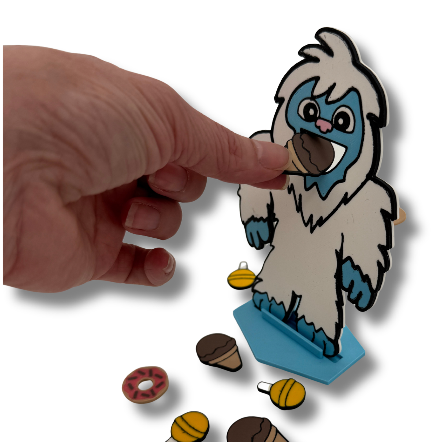 Hand placing feeding piece into yeti mouth showing how the interactive game works